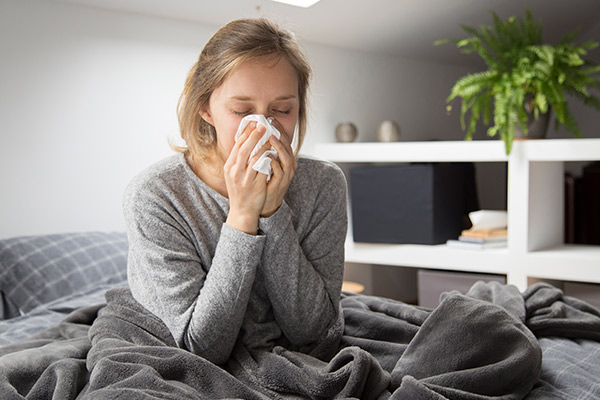Sick woman sitting in bed, blowing nose with napkin