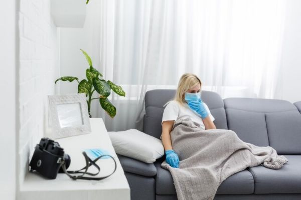 a women sitting on the sofa with gloves and mask